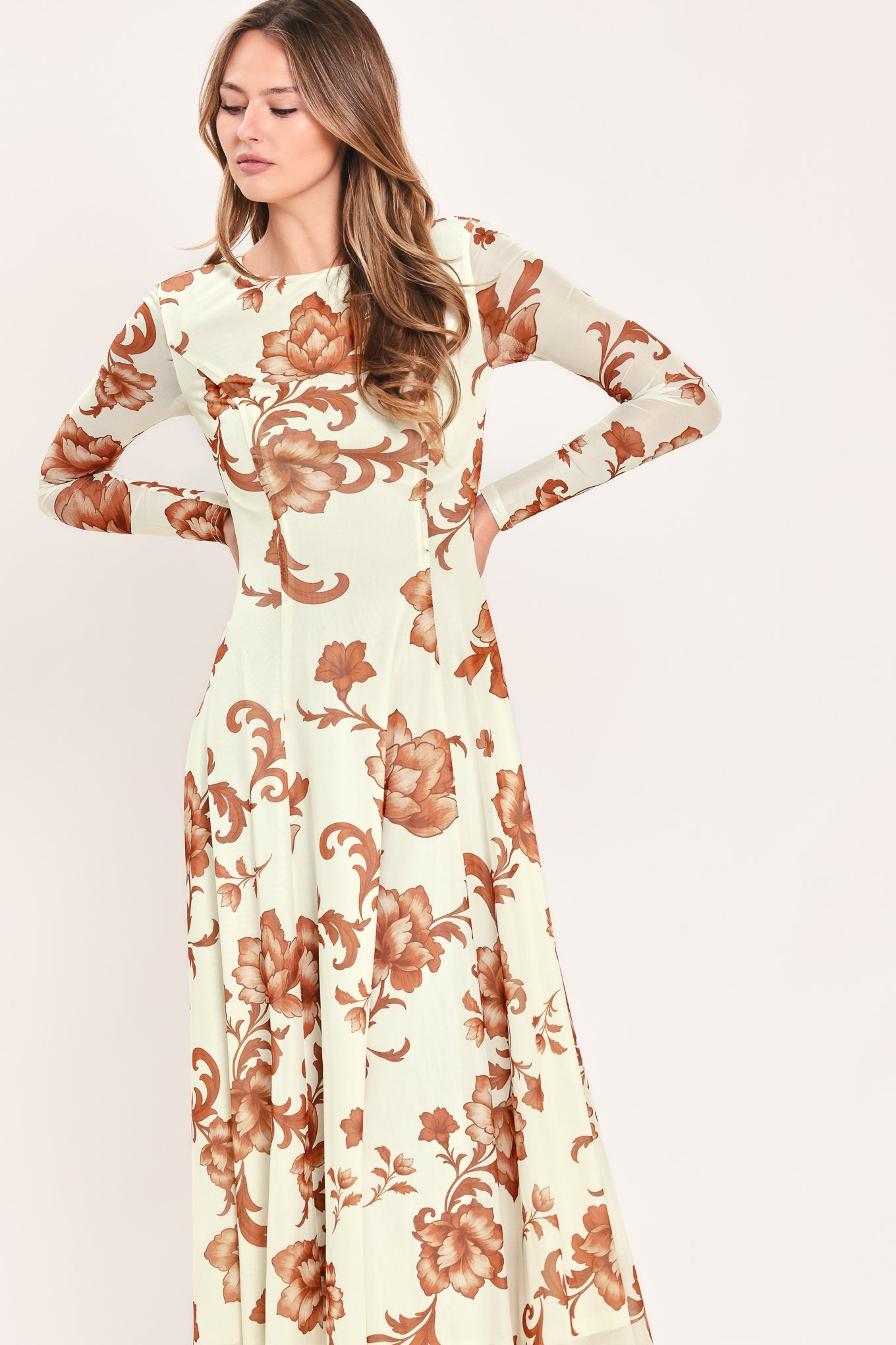 A woman wearing a long-sleeve midi dress with a cream base and a brown baroque-style floral pattern | Flying Tomato