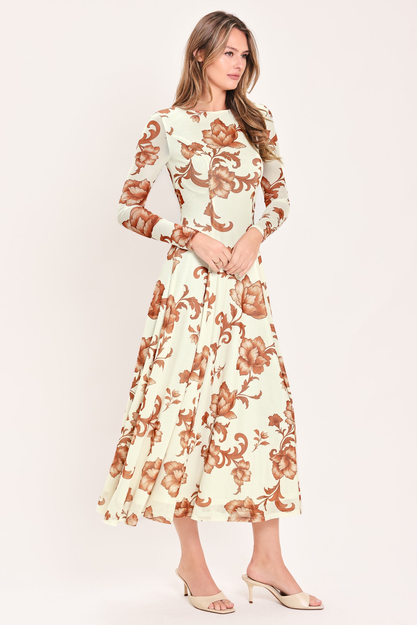 A woman wearing a long-sleeve midi dress with a cream base and a brown baroque-style floral pattern | Flying Tomato