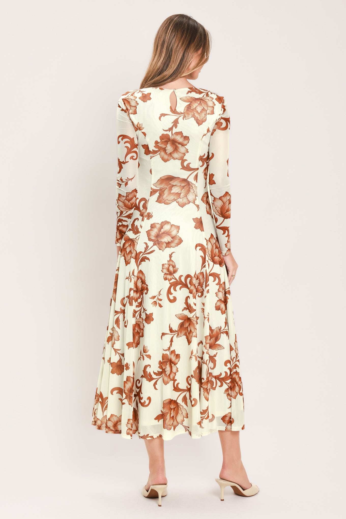 A woman wearing a long-sleeve midi dress with a cream base and a brown baroque-style floral pattern | Flying Tomato