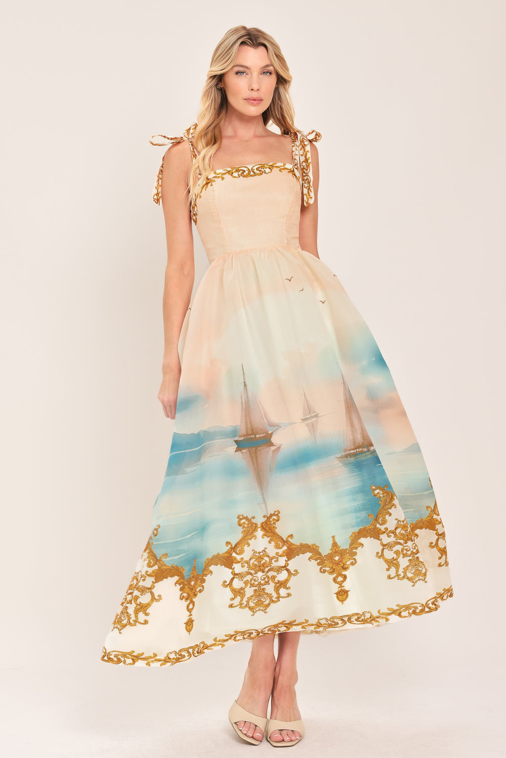 Woman wearing a long, elegant dress with sail boats and gold details featuring a straight neckline, shoulder tie, full skirt and smocked back bodice | Flying Tomato