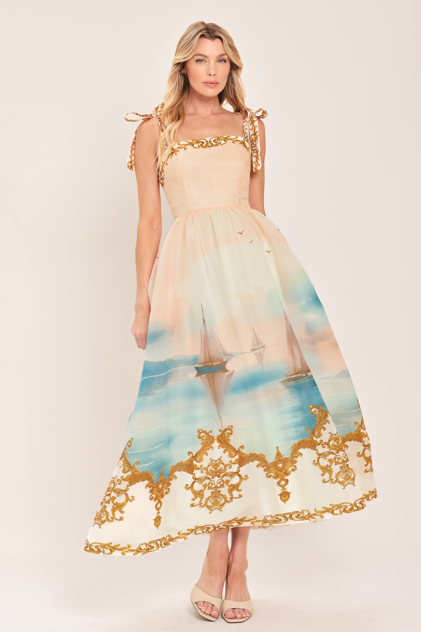 Woman wearing a long, elegant dress with sail boats and gold details featuring a straight neckline, shoulder tie, full skirt and smocked back bodice | Flying Tomato