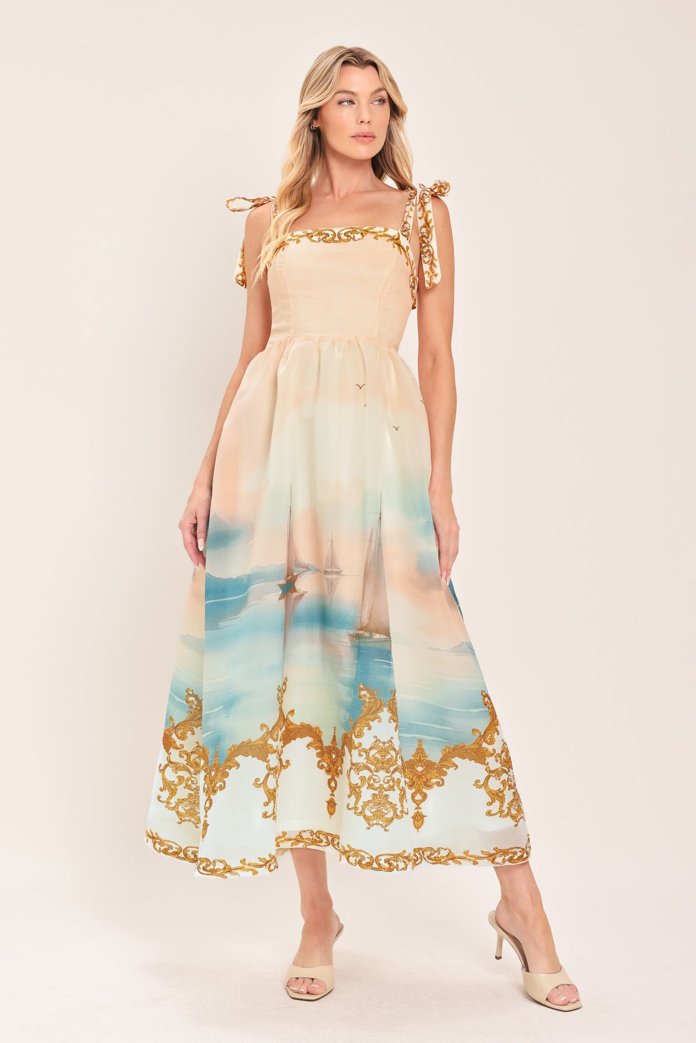 Woman wearing a long, elegant dress with sail boats and gold details featuring a straight neckline, shoulder tie, full skirt and smocked back bodice | Flying Tomato