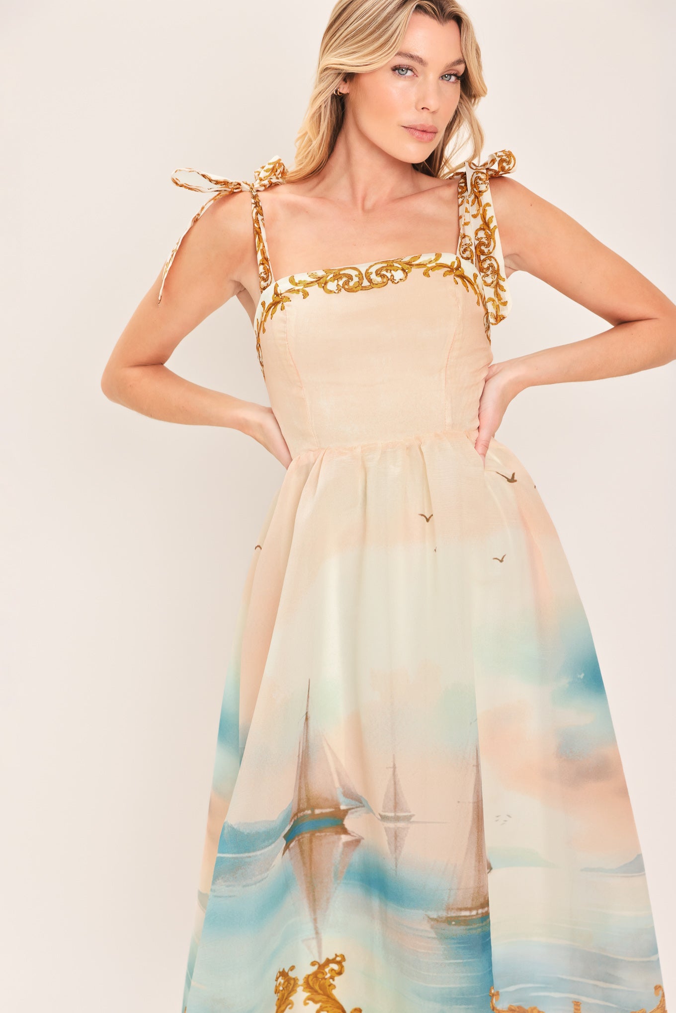 Woman wearing a long, elegant dress with sail boats and gold details featuring a straight neckline, shoulder tie, full skirt and smocked back bodice | Flying Tomato