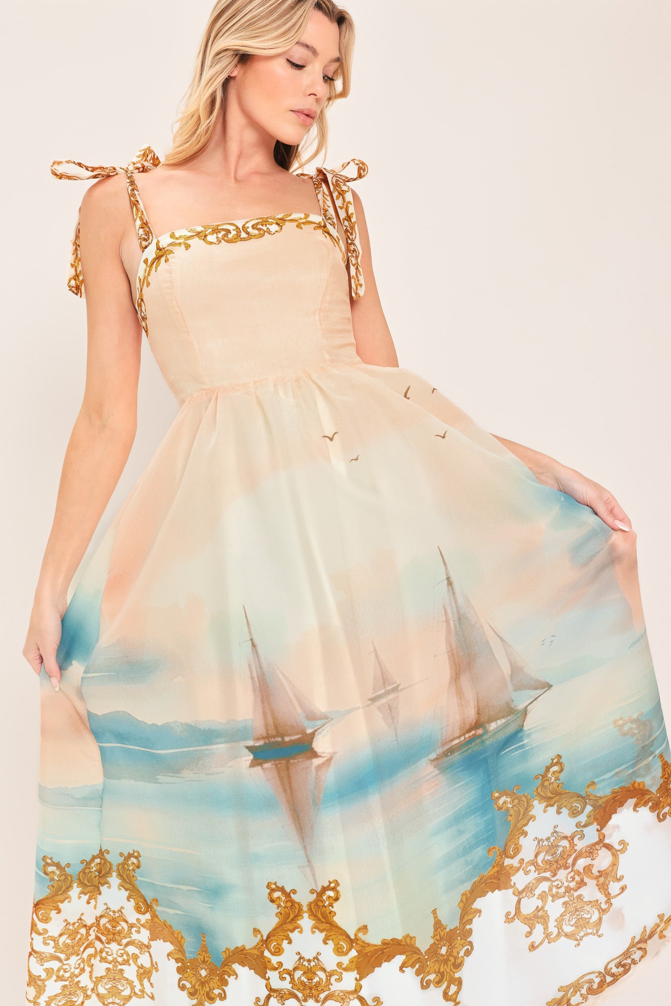 Woman wearing a long, elegant dress with sail boats and gold details featuring a straight neckline, shoulder tie, full skirt and smocked back bodice | Flying Tomato