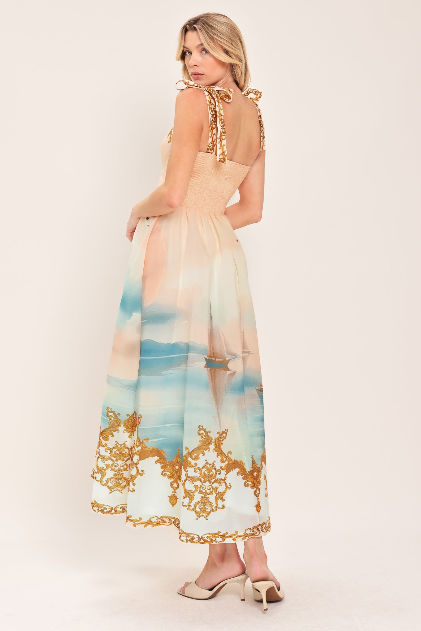 Woman wearing a long, elegant dress with sail boats and gold details featuring a straight neckline, shoulder tie, full skirt and smocked back bodice | Flying Tomato
