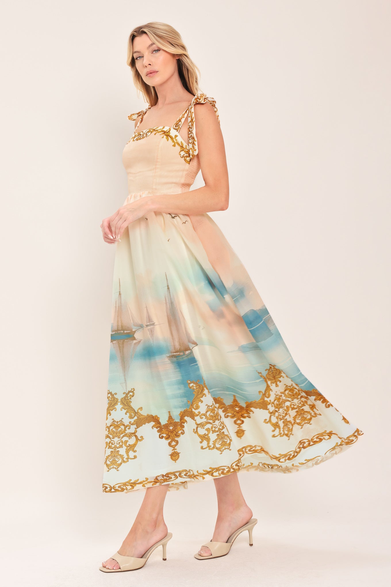 Woman wearing a long, elegant dress with sail boats and gold details featuring a straight neckline, shoulder tie, full skirt and smocked back bodice | Flying Tomato