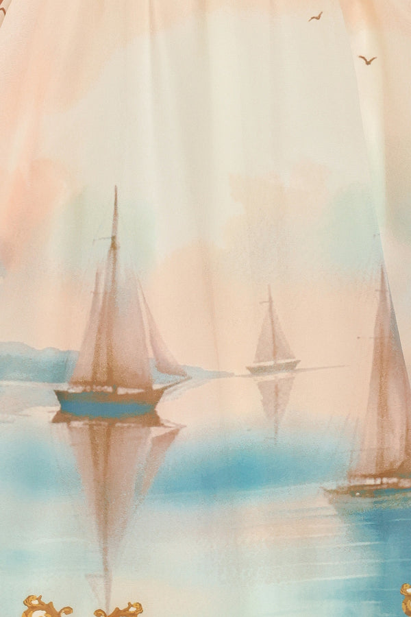 Close up of long, elegant dress with sail boats and gold details featuring a straight neckline, shoulder tie, full skirt and smocked back bodice | Flying Tomato