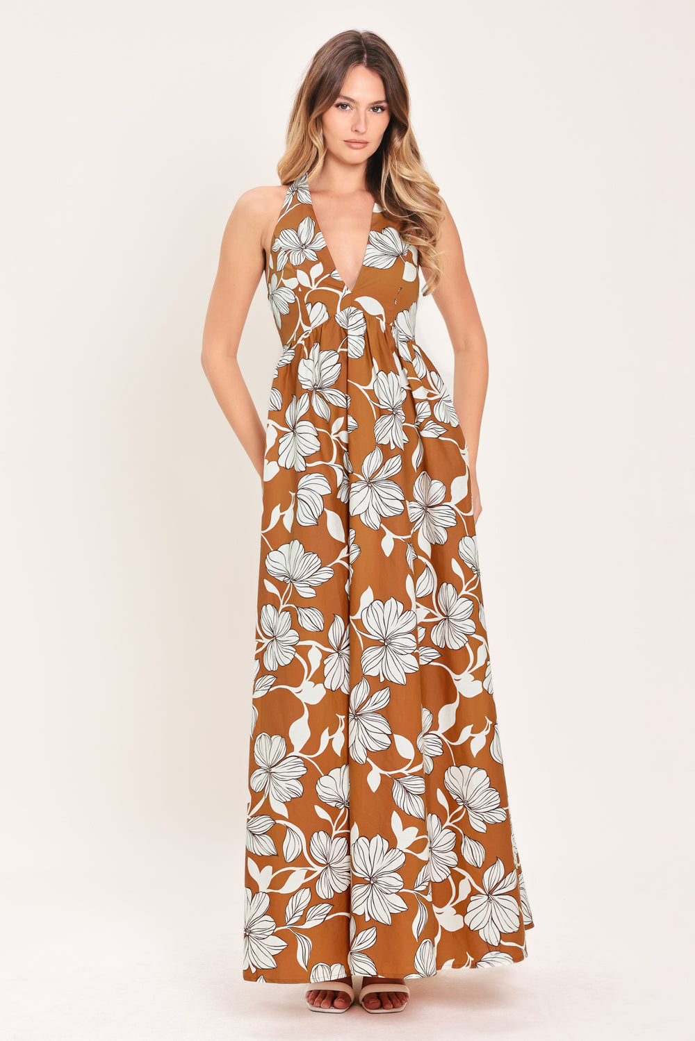Woman wearing a camel and white with black lineart floral maxi dress maxi dress featuring halter neckline with back neck tie, bare back and smocked bodice | Flying Tomato