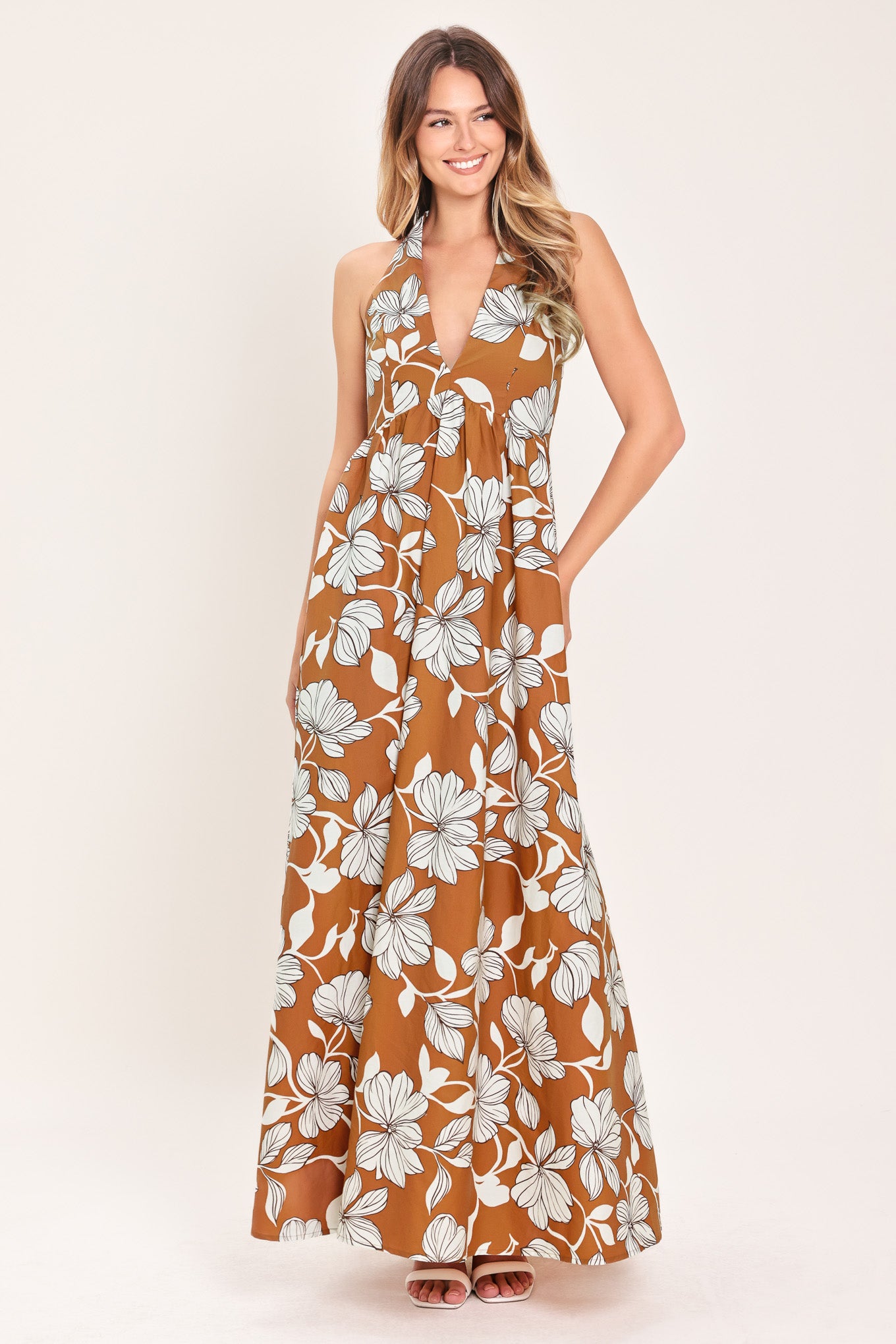 Woman wearing a camel and white with black lineart floral maxi dress maxi dress featuring halter neckline with back neck tie, bare back and smocked bodice | Flying Tomato