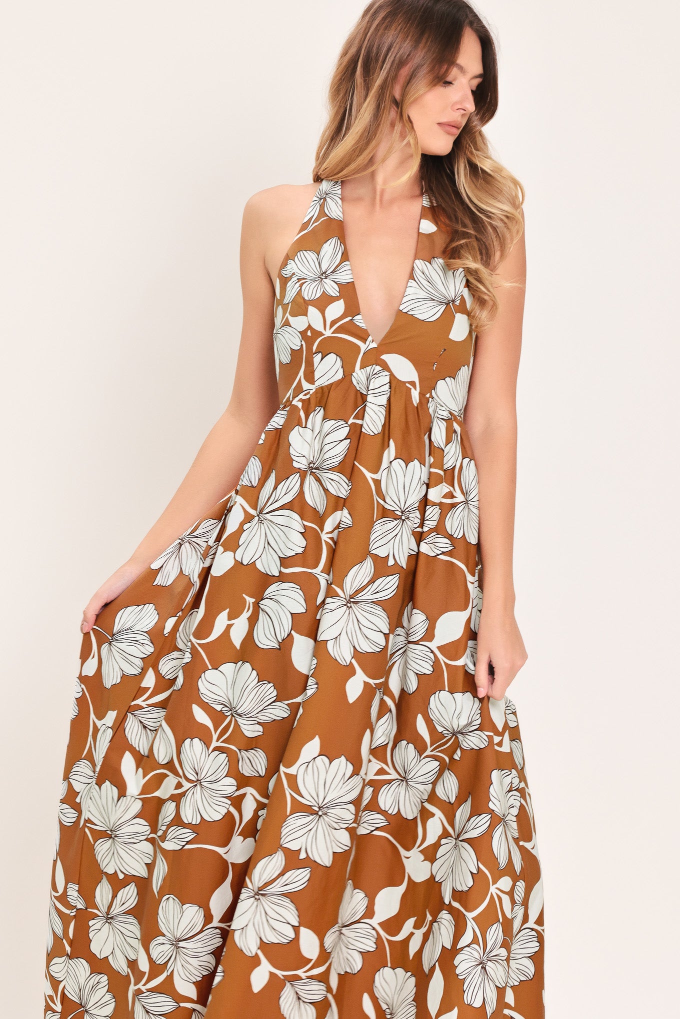 Woman wearing a camel and white with black lineart floral maxi dress maxi dress featuring halter neckline with back neck tie, bare back and smocked bodice | Flying Tomato