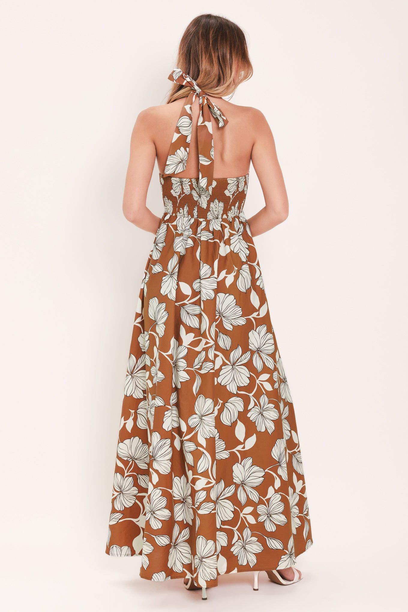 Woman wearing a camel and white with black lineart floral maxi dress maxi dress featuring halter neckline with back neck tie, bare back and smocked bodice | Flying Tomato