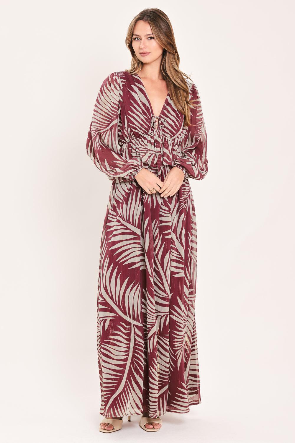 A woman wearing a long-sleeve maxi dress with a deep V-neck and a tropical palm leaf print in burgundy and cream | Flying Tomato