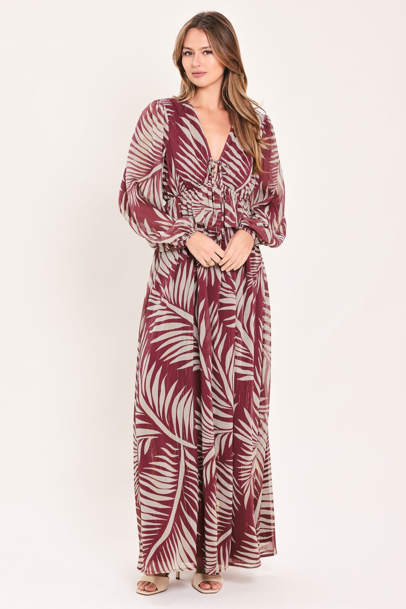 A woman wearing a long-sleeve maxi dress with a deep V-neck and a tropical palm leaf print in burgundy and cream | Flying Tomato