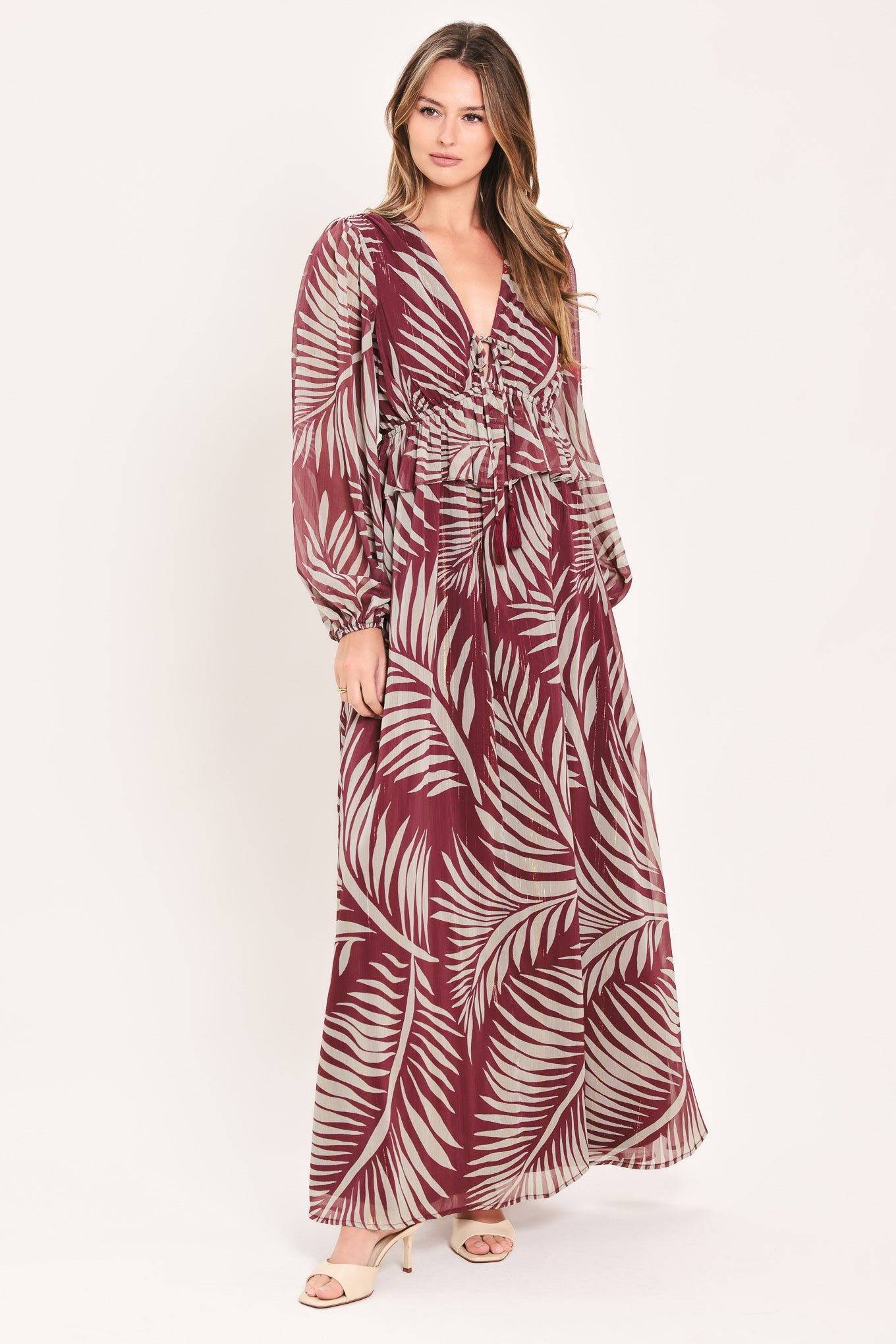 A woman wearing a long-sleeve maxi dress with a deep V-neck and a tropical palm leaf print in burgundy and cream | Flying Tomato
