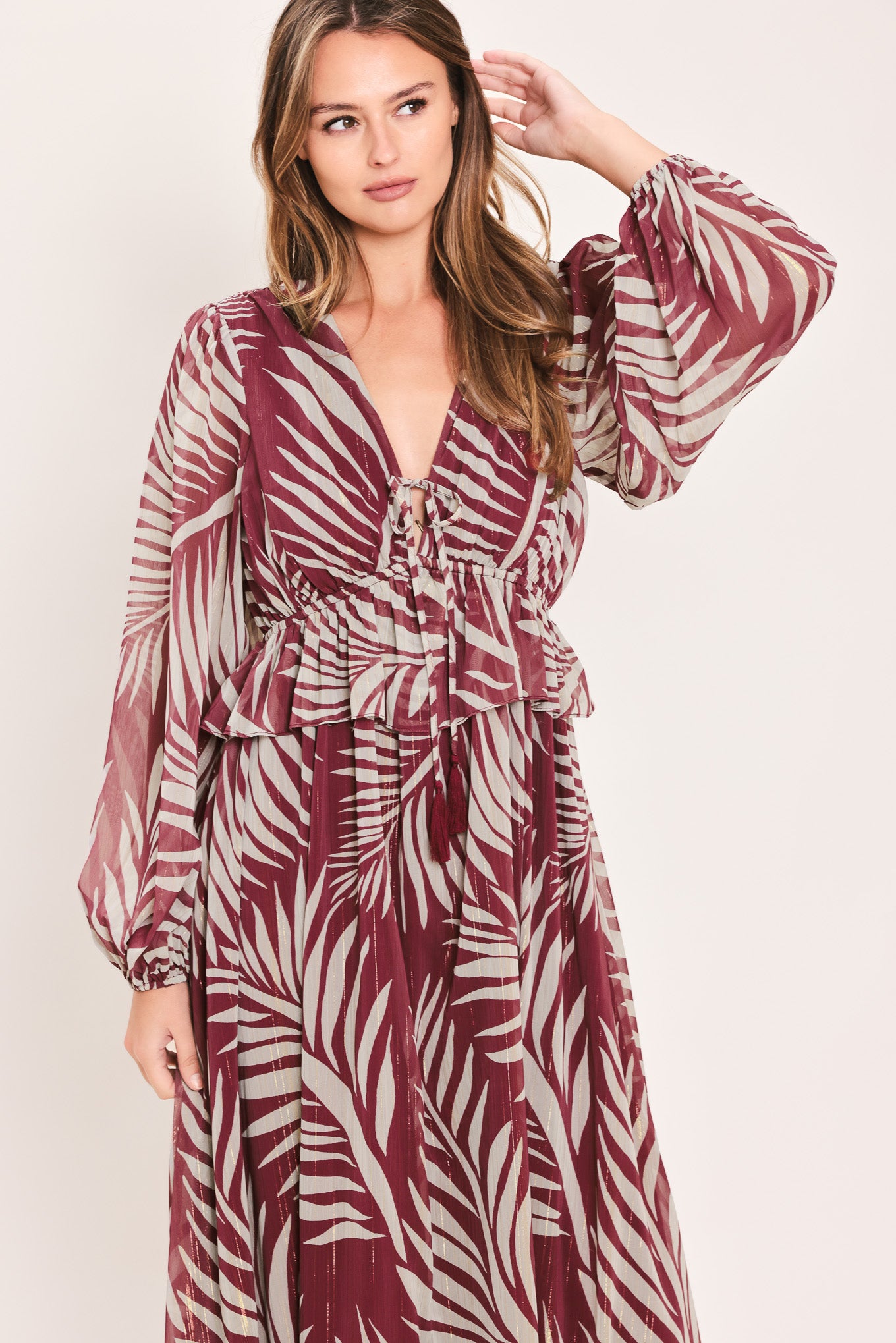 A woman wearing a long-sleeve maxi dress with a deep V-neck and a tropical palm leaf print in burgundy and cream | Flying Tomato