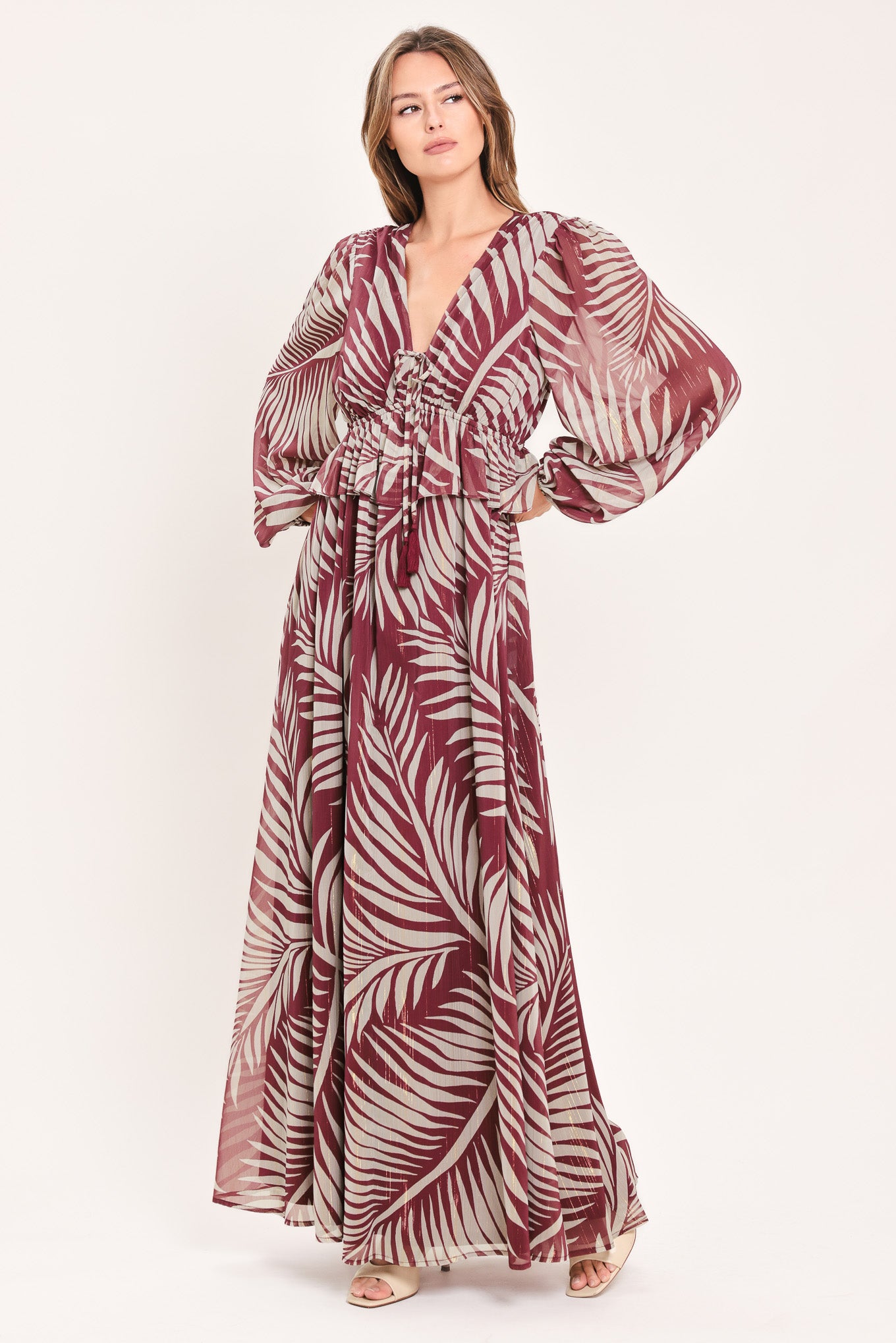 A woman wearing a long-sleeve maxi dress with a deep V-neck and a tropical palm leaf print in burgundy and cream | Flying Tomato