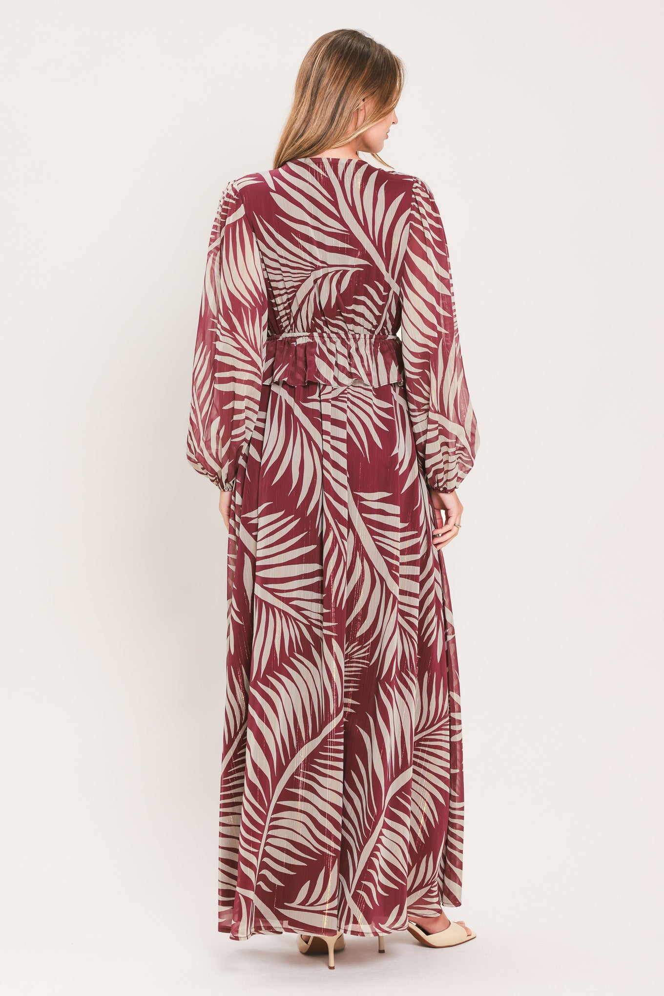 A woman wearing a long-sleeve maxi dress with a deep V-neck and a tropical palm leaf print in burgundy and cream | Flying Tomato