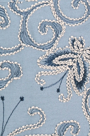 Close-up of embroidered fabric with blue and white floral patterns on a light blue fabric | Flying Tomato