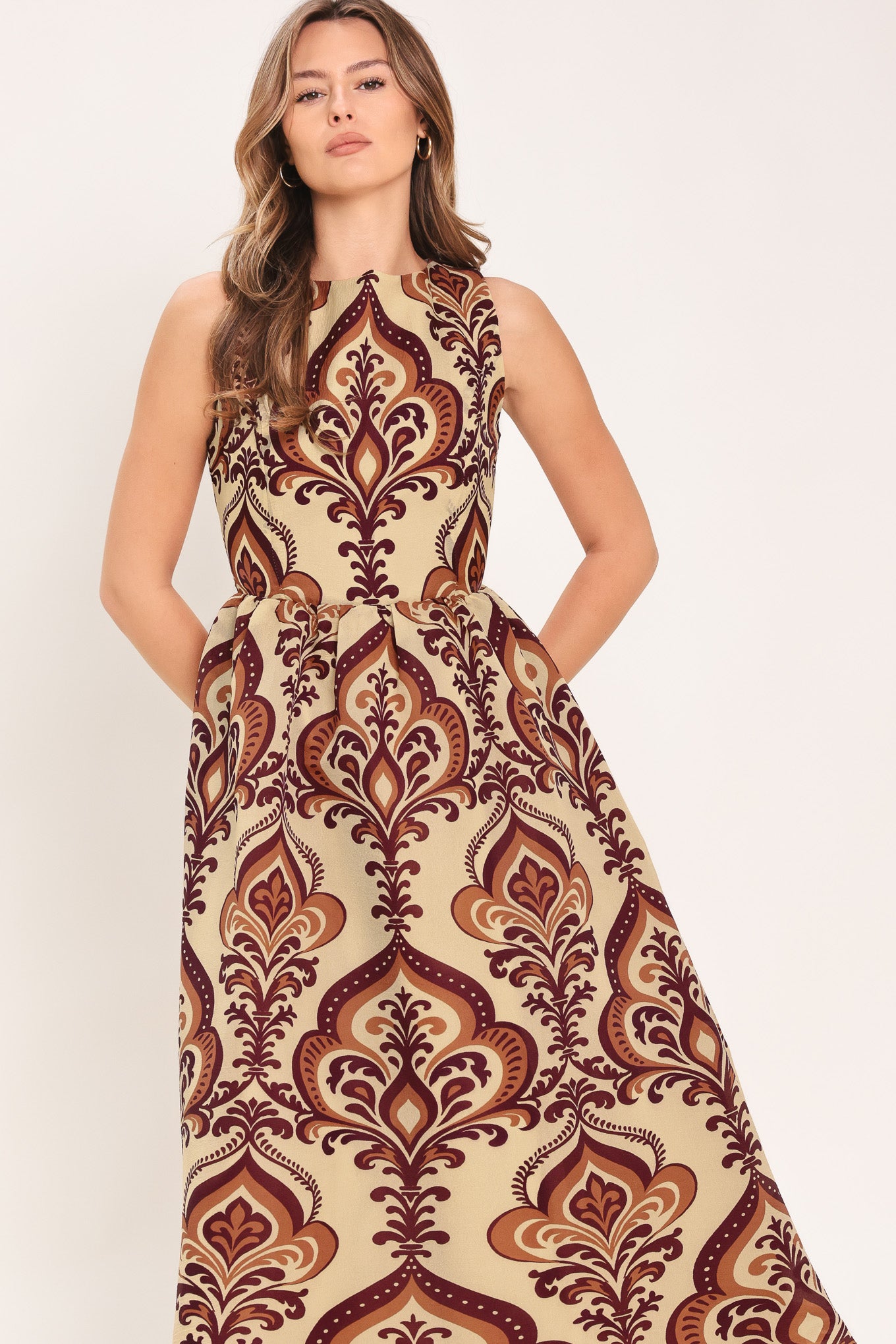 Woman wearing a taupe patterned  midi dress featuring round neckline, sleeveless, full skirt and back zipper closure | Flying Tomato