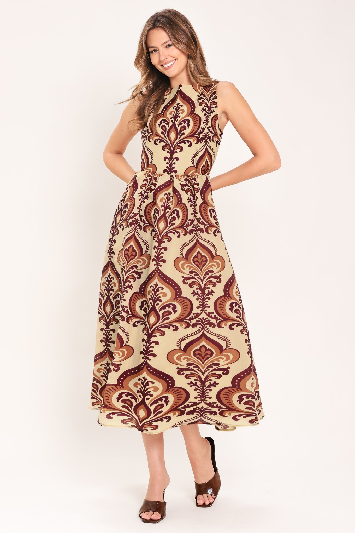 Woman wearing a taupe patterned  midi dress featuring round neckline, sleeveless, full skirt and back zipper closure | Flying Tomato