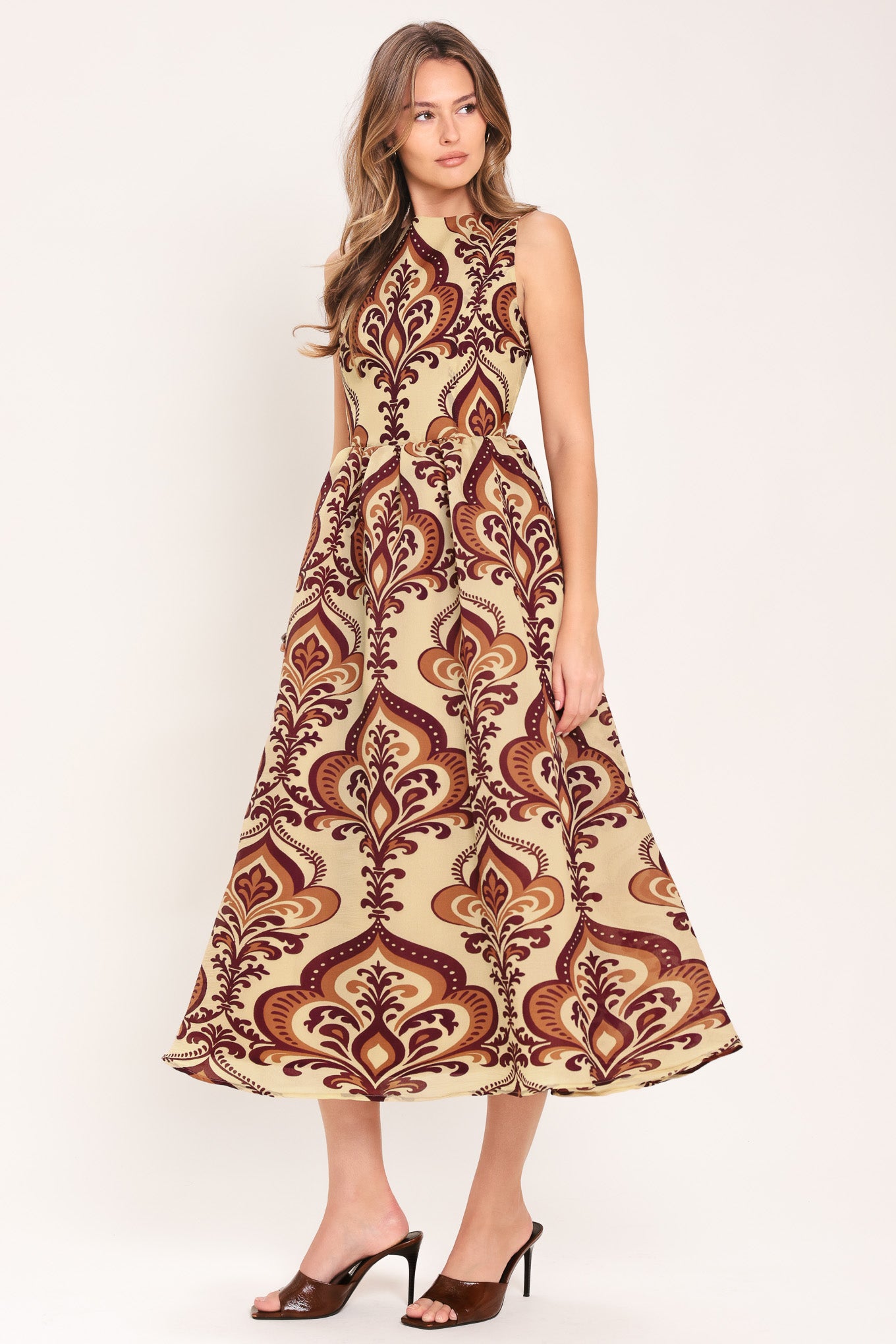 Woman wearing a taupe patterned  midi dress featuring round neckline, sleeveless, full skirt and back zipper closure | Flying Tomato