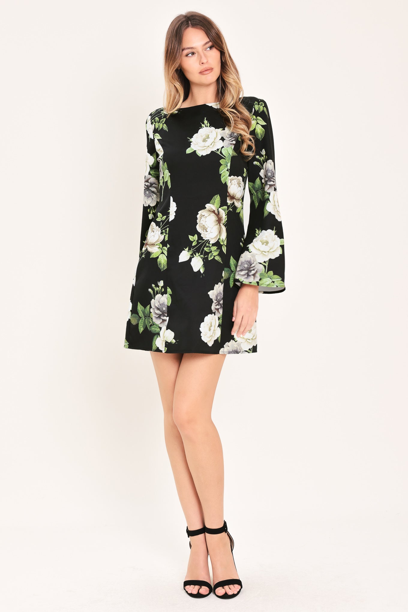 Woman wearing a black with white floral pattern mini dress with wide neckline, long bell sleeve and back zipper closure | Flying Tomato