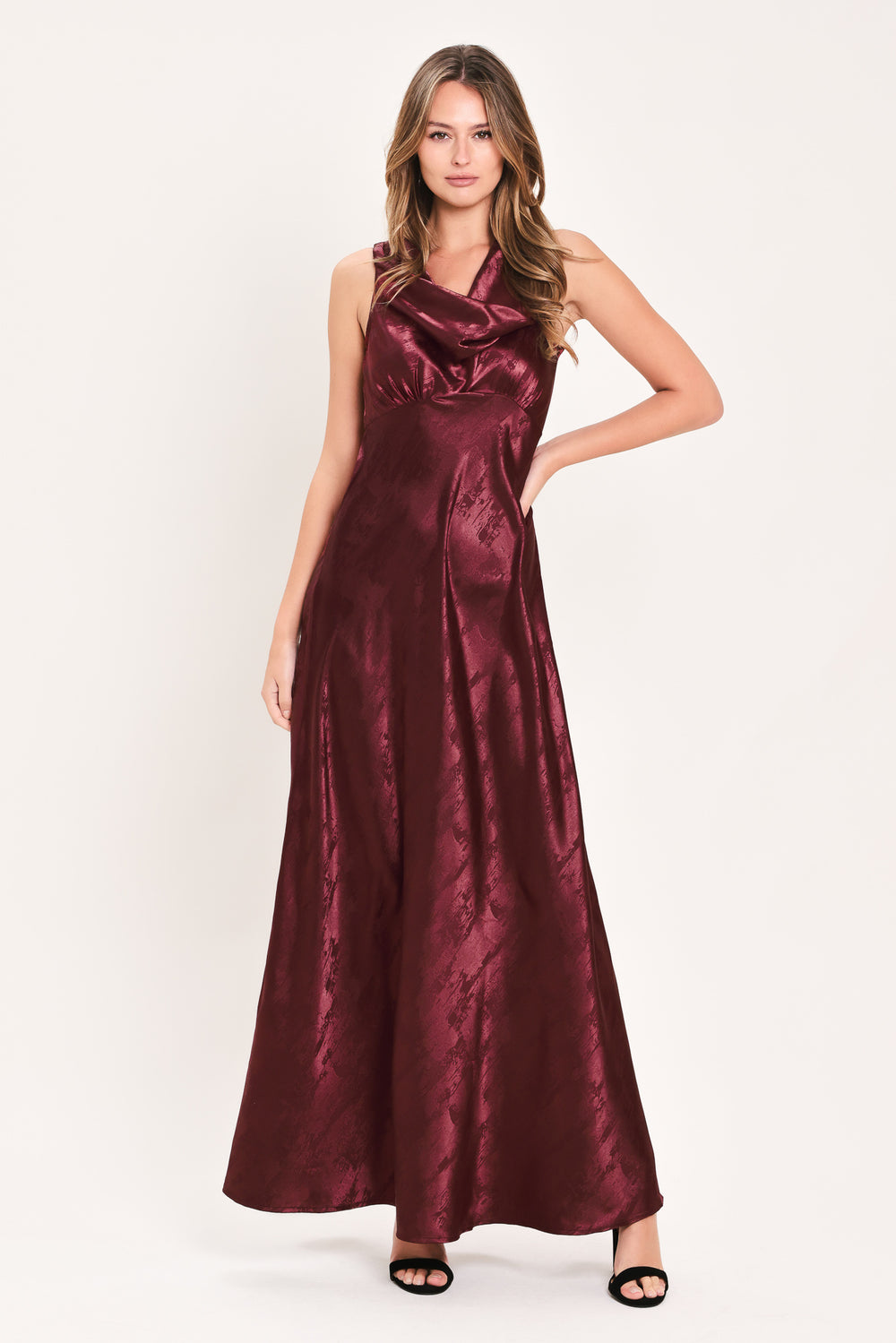 A woman wearing a sleeveless, floor-length metallic burgundy gown with a draped neckline and a subtle crinkle texture | Flying Tomato