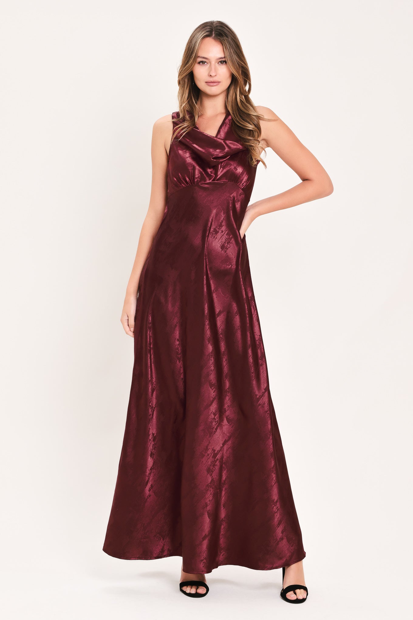 A woman wearing a sleeveless, floor-length metallic burgundy gown with a draped neckline and a subtle crinkle texture | Flying Tomato