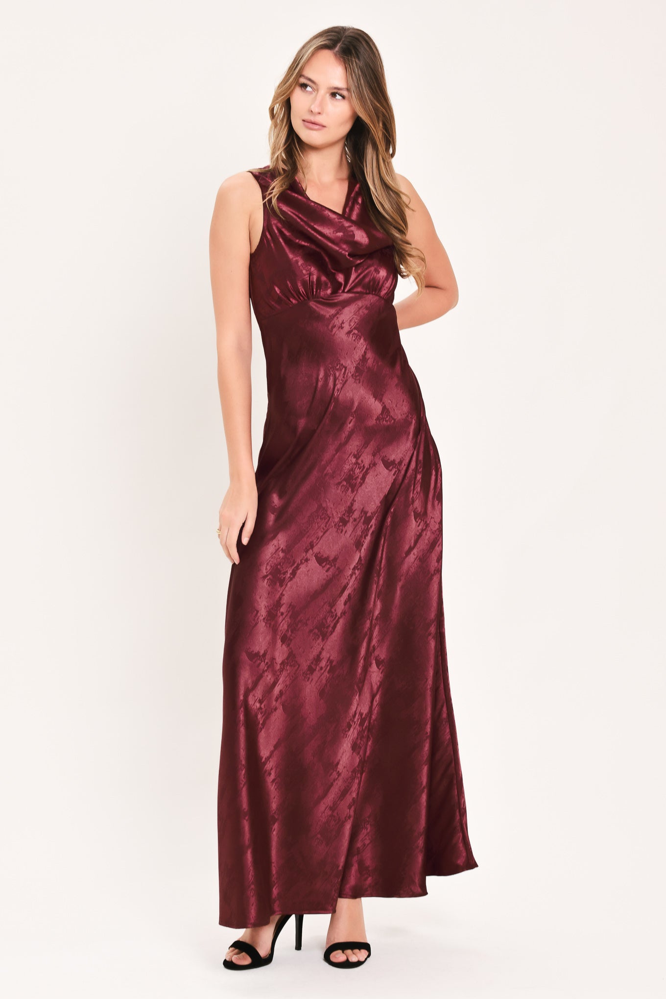 A woman wearing a sleeveless, floor-length metallic burgundy gown with a draped neckline and a subtle crinkle texture | Flying Tomato