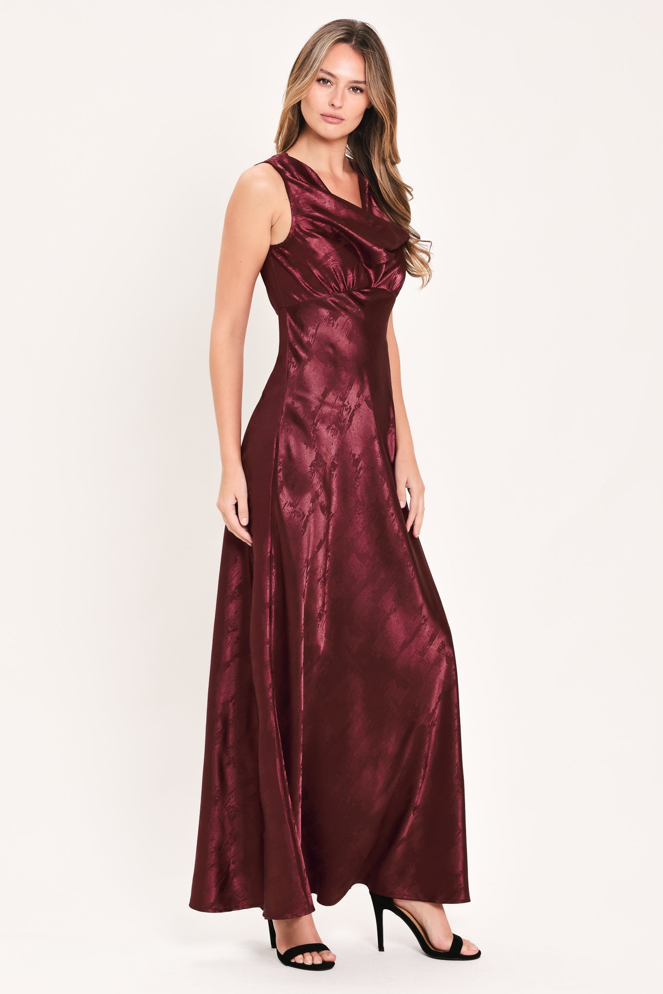 A woman wearing a sleeveless, floor-length metallic burgundy gown with a draped neckline and a subtle crinkle texture | Flying Tomato