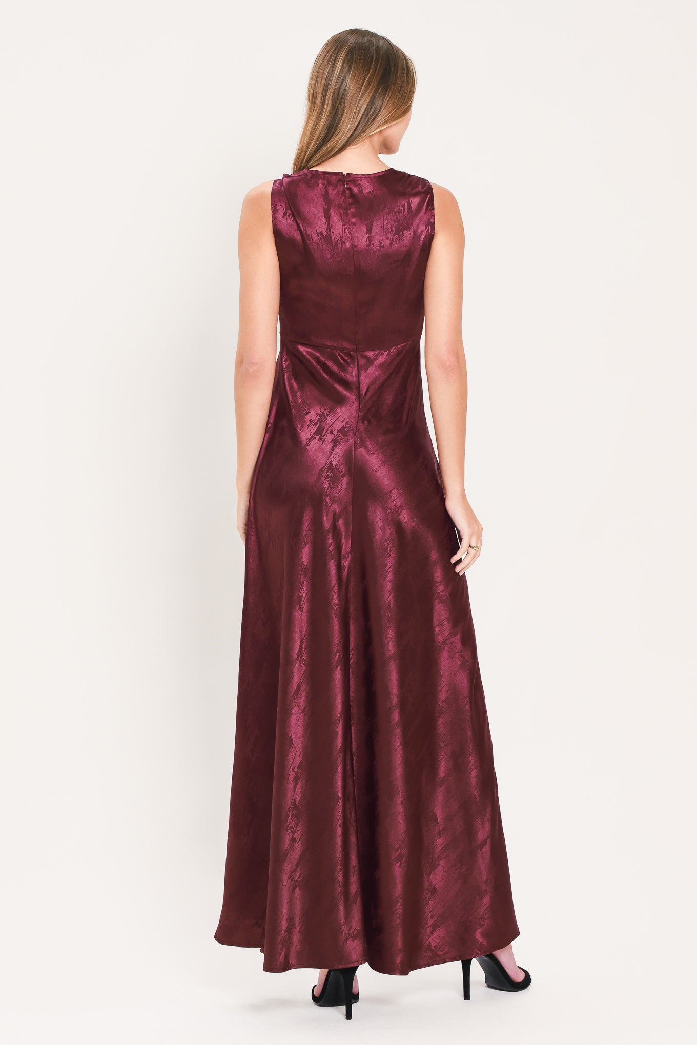 A woman wearing a sleeveless, floor-length metallic burgundy gown with a draped neckline and a subtle crinkle texture | Flying Tomato