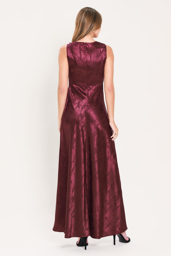 A woman wearing a sleeveless, floor-length metallic burgundy gown with a draped neckline and a subtle crinkle texture | Flying Tomato