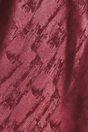 A woman wearing a sleeveless, floor-length metallic burgundy gown with a draped neckline and a subtle crinkle texture | Flying Tomato