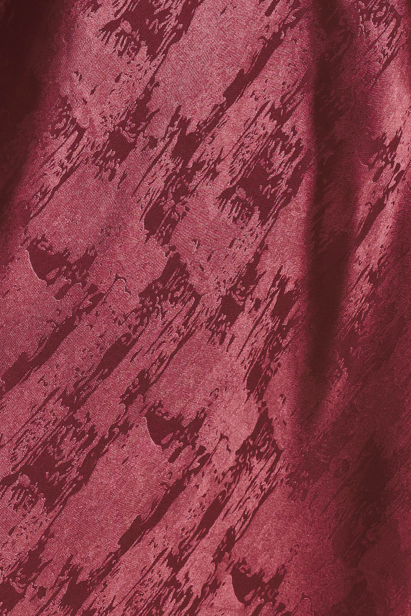 A woman wearing a sleeveless, floor-length metallic burgundy gown with a draped neckline and a subtle crinkle texture | Flying Tomato