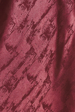 A woman wearing a sleeveless, floor-length metallic burgundy gown with a draped neckline and a subtle crinkle texture | Flying Tomato