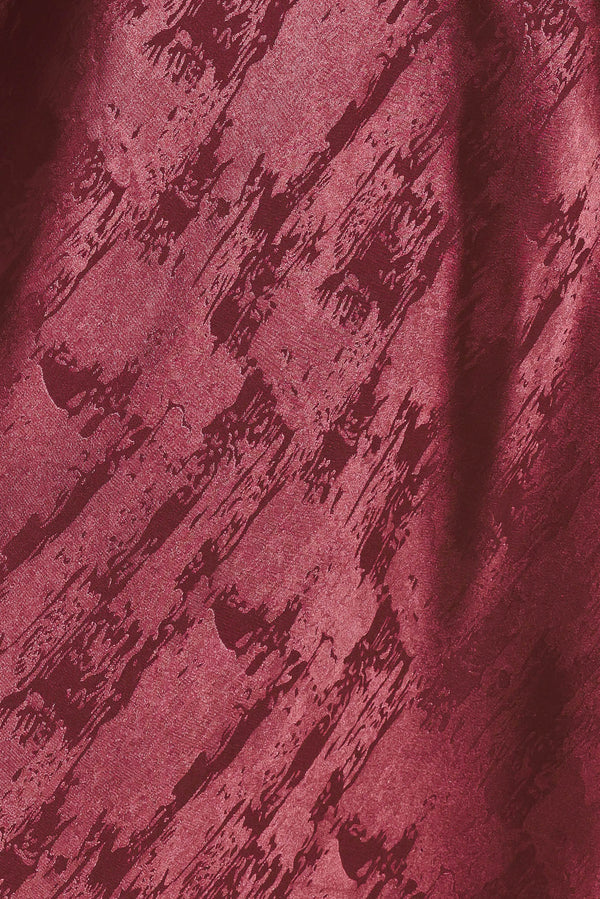 A woman wearing a sleeveless, floor-length metallic burgundy gown with a draped neckline and a subtle crinkle texture | Flying Tomato