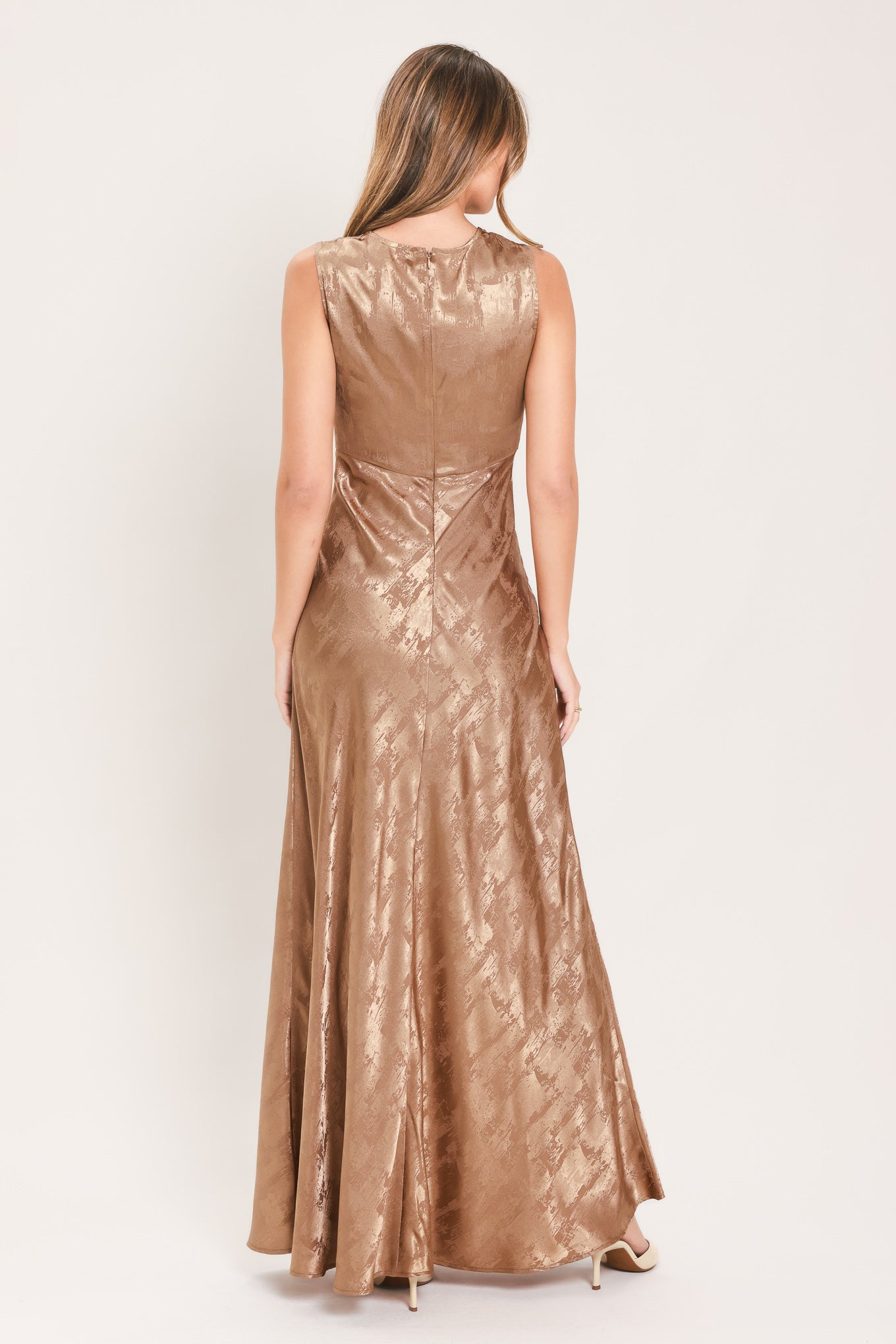 A woman wearing a sleeveless, floor-length metallic champagne-gold gown with a draped neckline and a subtle crinkle texture | Flying Tomato