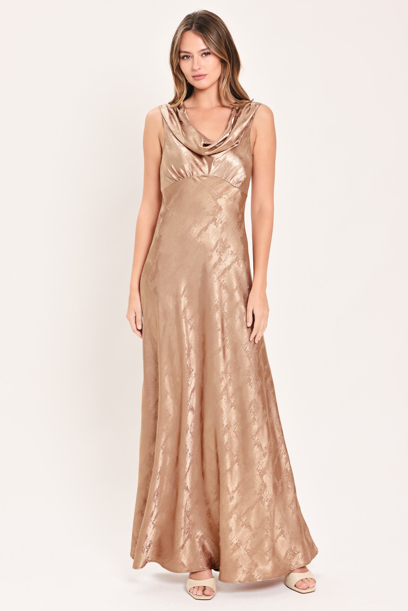 A woman wearing a sleeveless, floor-length metallic champagne-gold gown with a draped neckline and a subtle crinkle texture | Flying Tomato