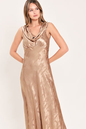 A woman wearing a sleeveless, floor-length metallic champagne-gold gown with a draped neckline and a subtle crinkle texture | Flying Tomato
