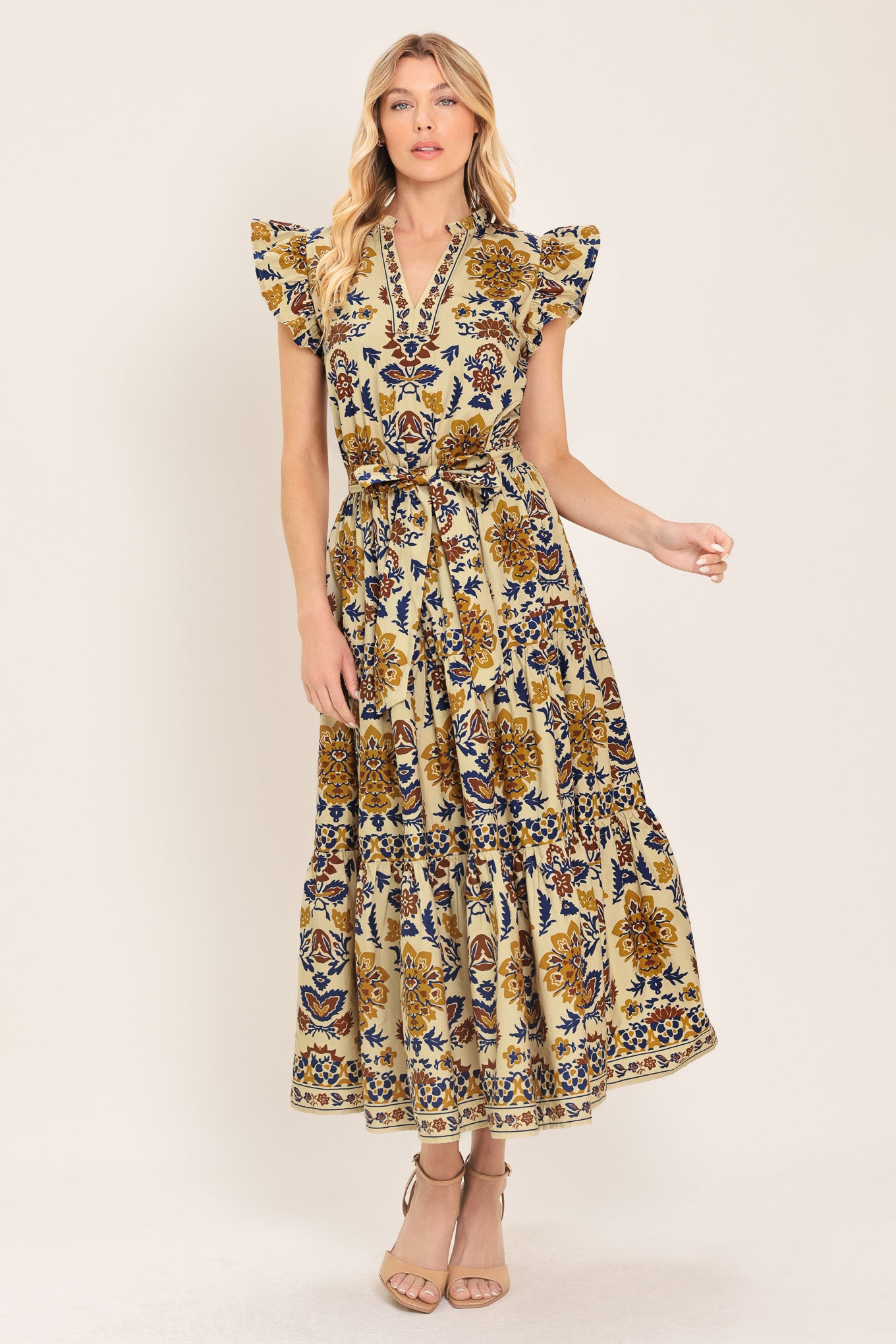 Woman wearing a taupe printed midi dress featuring V neckline with ruffled edge, short ruffle sleeve, elastic waist, self sash and tier skirt | Flying Tomato