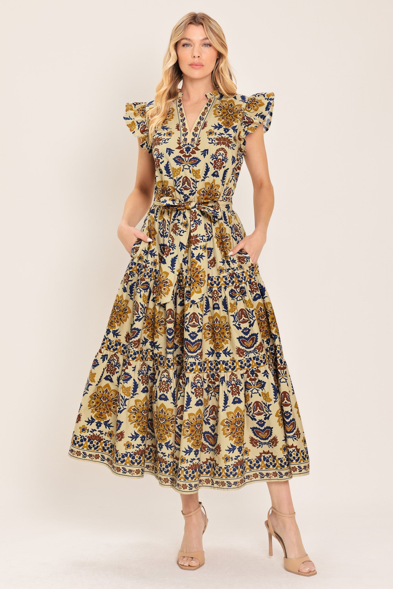 Woman wearing a taupe printed midi dress featuring V neckline with ruffled edge, short ruffle sleeve, elastic waist, self sash and tier skirt | Flying Tomato