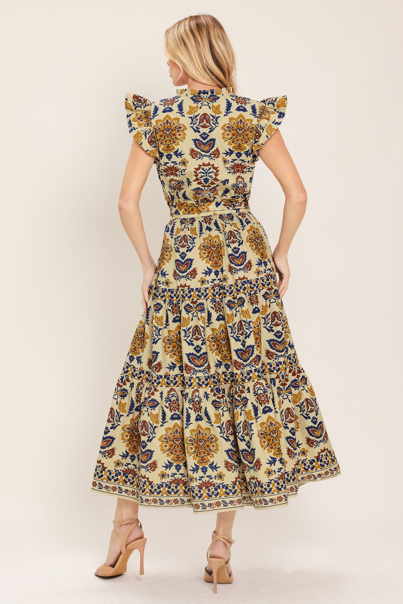 Woman wearing a taupe printed midi dress featuring V neckline with ruffled edge, short ruffle sleeve, elastic waist, self sash and tier skirt | Flying Tomato
