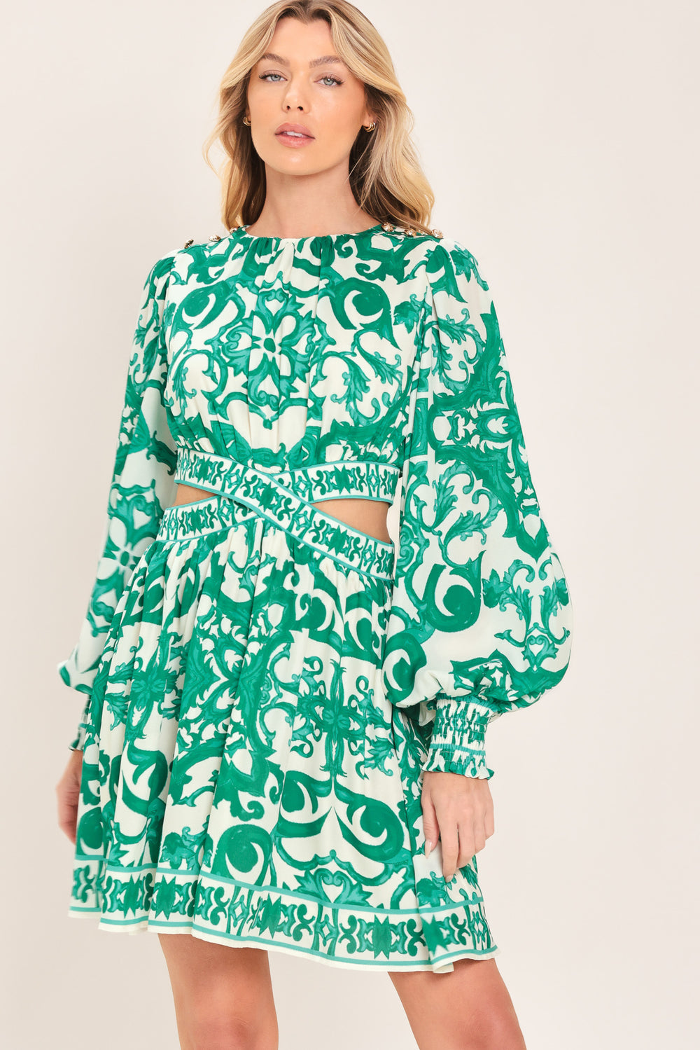 A woman wearing a green and white patterned long-sleeve mini dress with a tie waist and side cutouts| Flying Tomato