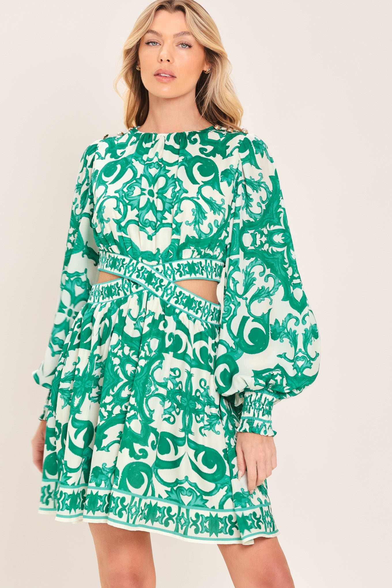 A woman wearing a green and white patterned long-sleeve mini dress with a tie waist and side cutouts| Flying Tomato
