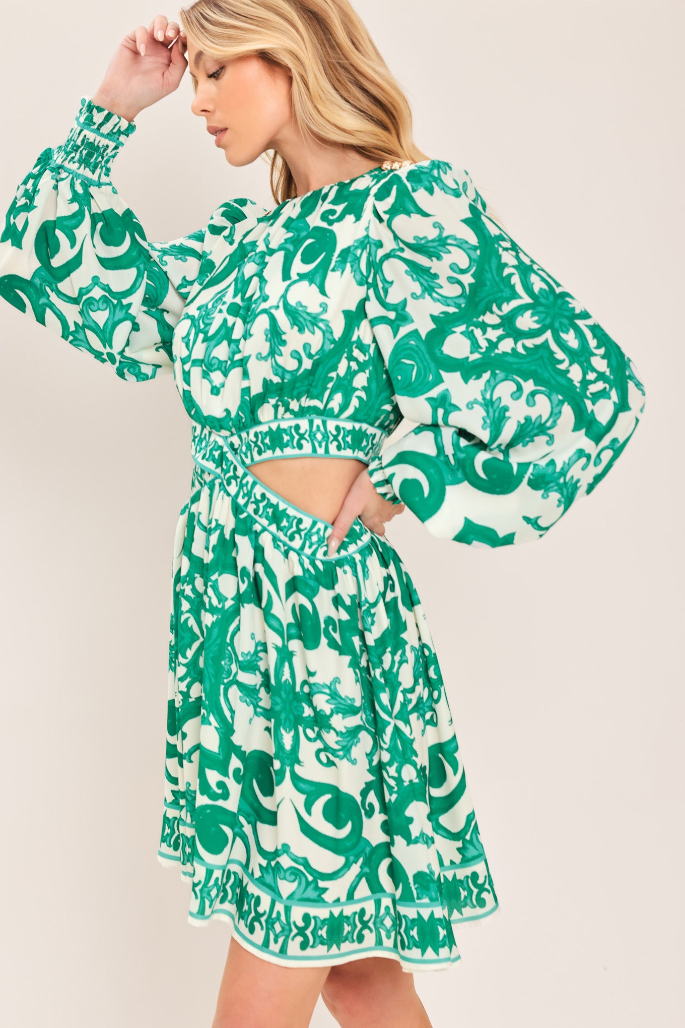 A woman wearing a green and white patterned long-sleeve mini dress with a tie waist and side cutouts| Flying Tomato