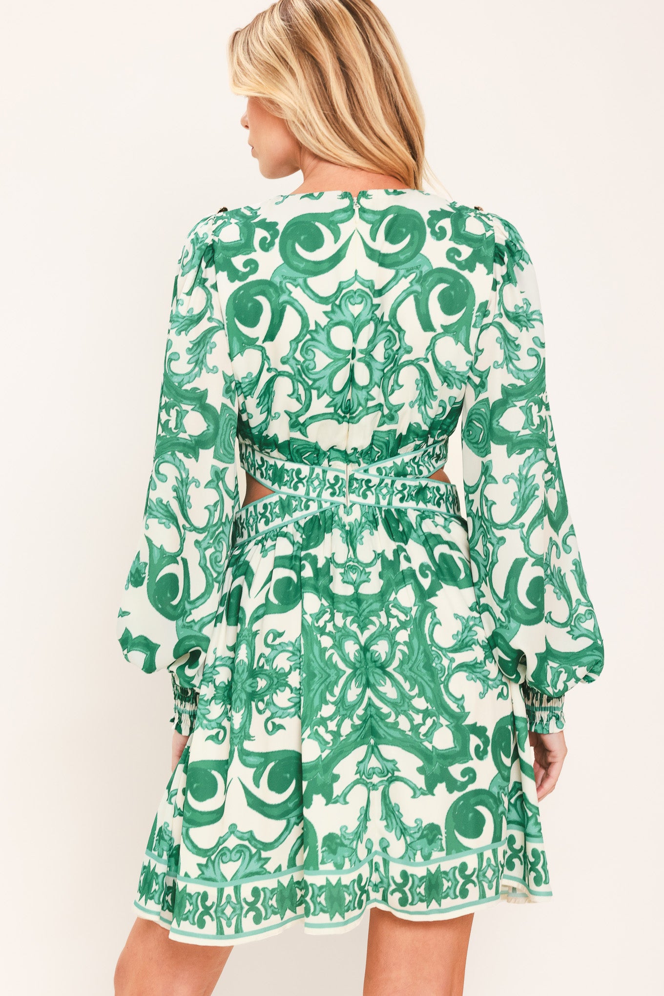A woman wearing a green and white patterned long-sleeve mini dress with a tie waist and side cutouts| Flying Tomato