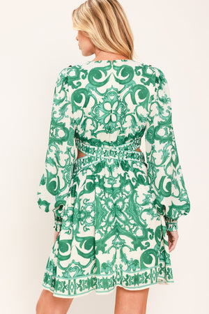 A woman wearing a green and white patterned long-sleeve mini dress with a tie waist and side cutouts| Flying Tomato