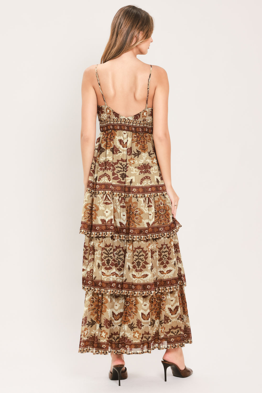 A woman modeling a sleeveless, tiered maxi dress with a bohemian-style floral and geometric pattern in brown and beige | Flying Tomato