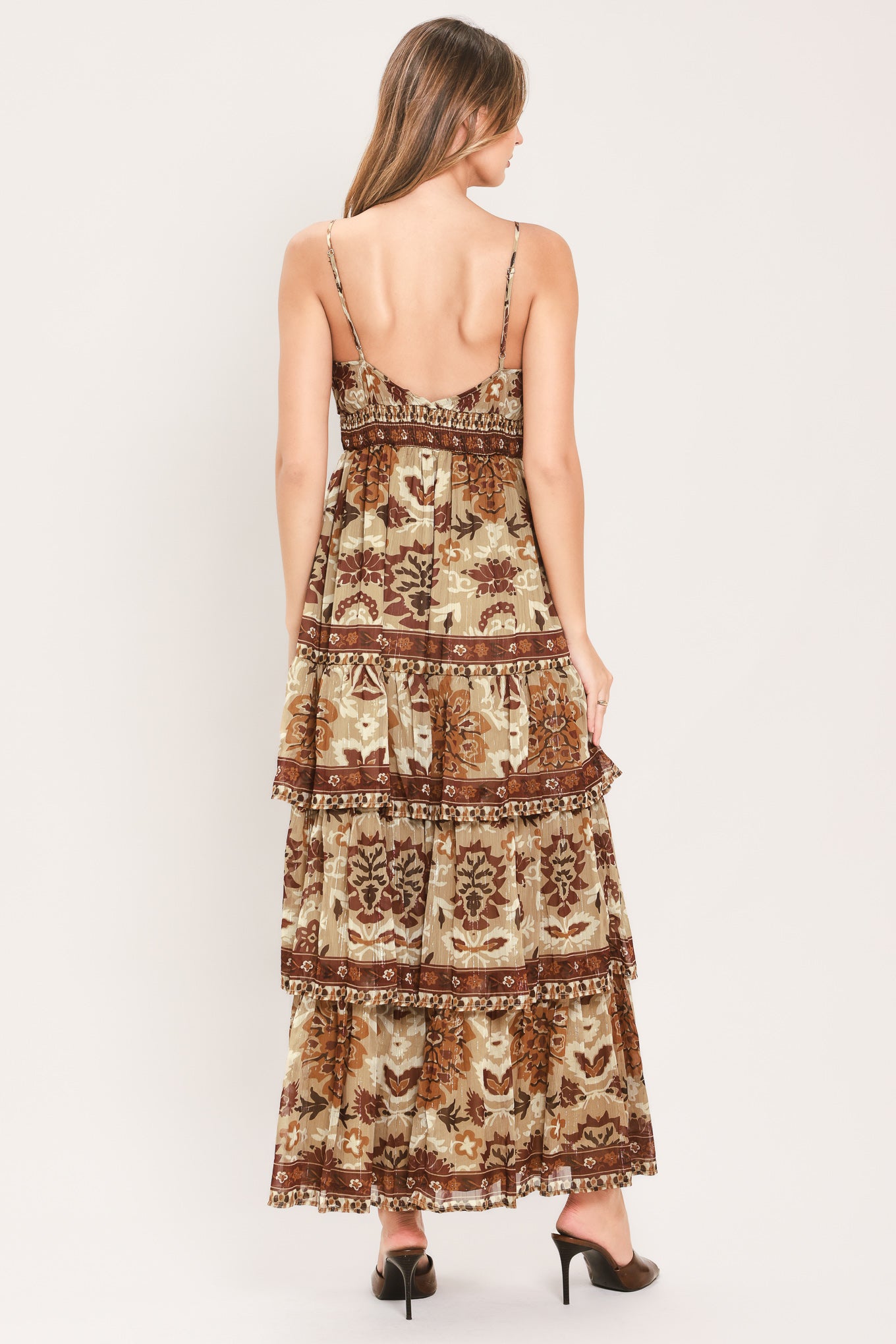 A woman modeling a sleeveless, tiered maxi dress with a bohemian-style floral and geometric pattern in brown and beige | Flying Tomato