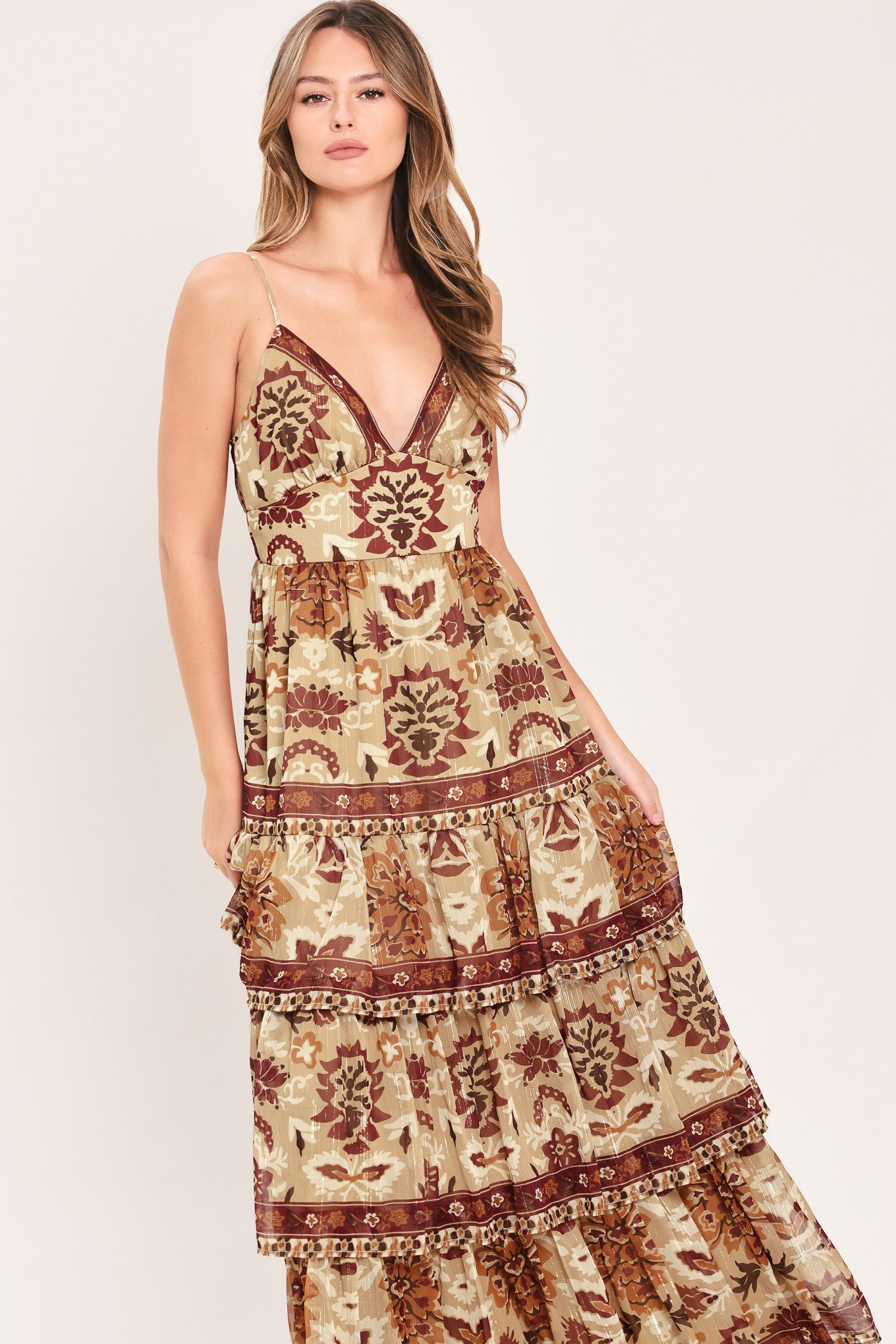 A woman modeling a sleeveless, tiered maxi dress with a bohemian-style floral and geometric pattern in brown and beige | Flying Tomato